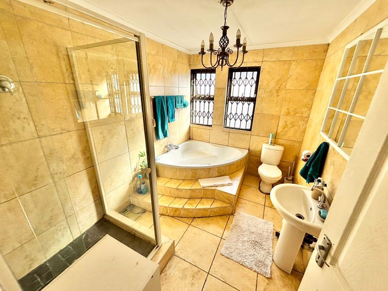A dated bathroom featuring a corner bathtub on a raised platform, a separate glass shower enclosure, pedestal basin, and full-height wall tiling.