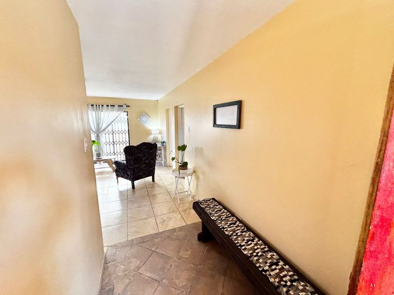 A bright hallway featuring tiled flooring, leading into an open-plan living area with access to a security gate.