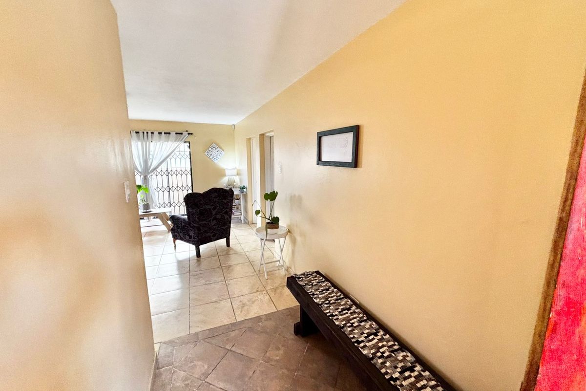 A bright hallway featuring tiled flooring, leading into an open-plan living area with access to a security gate.