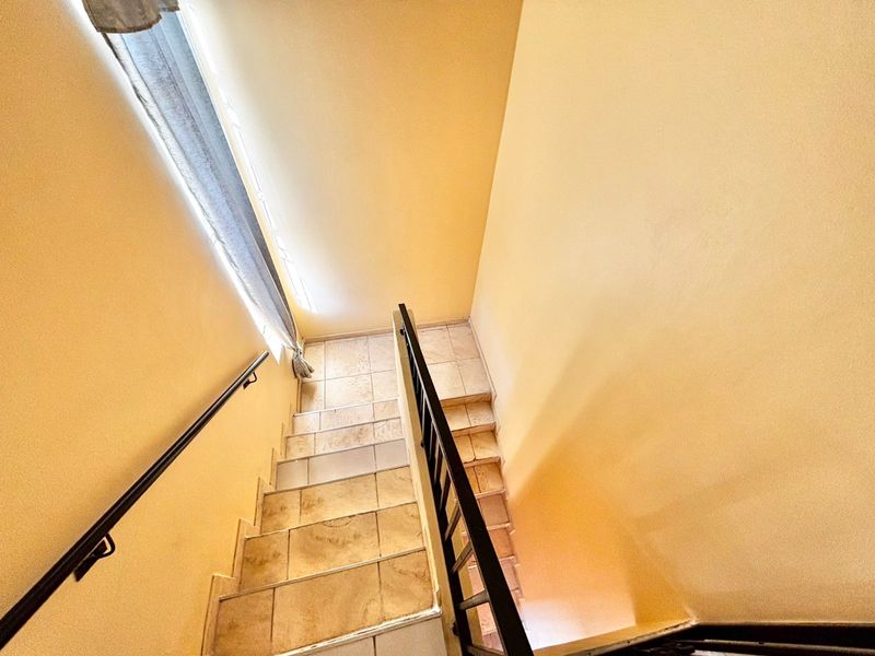 A view looking down a tiled staircase featuring a metal handrail and balustrade, connecting different levels of the townhouse.