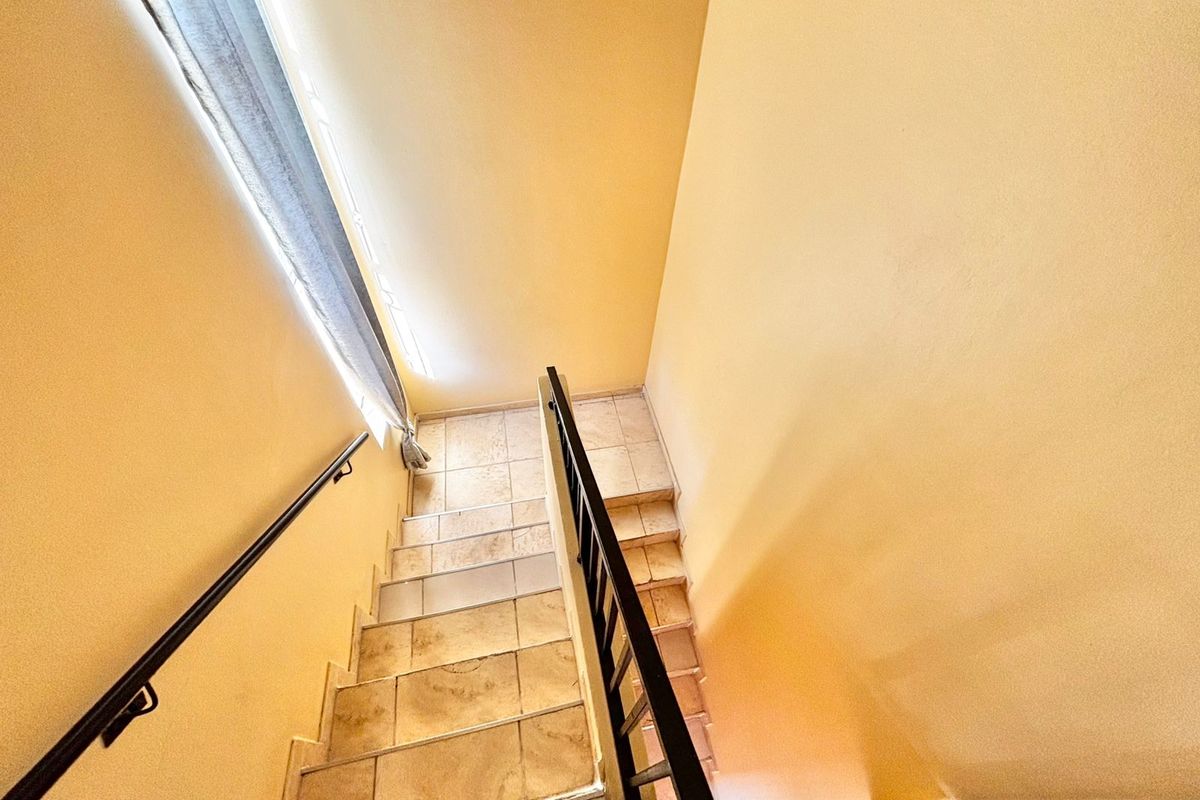 A view looking down a tiled staircase featuring a metal handrail and balustrade, connecting different levels of the townhouse.
