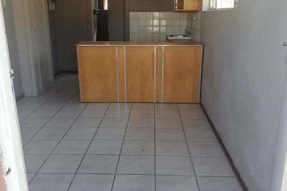 An empty kitchen area featuring tiled flooring, built-in cabinetry with a sink, and a tiled splashback, offering a blank canvas for renovation.