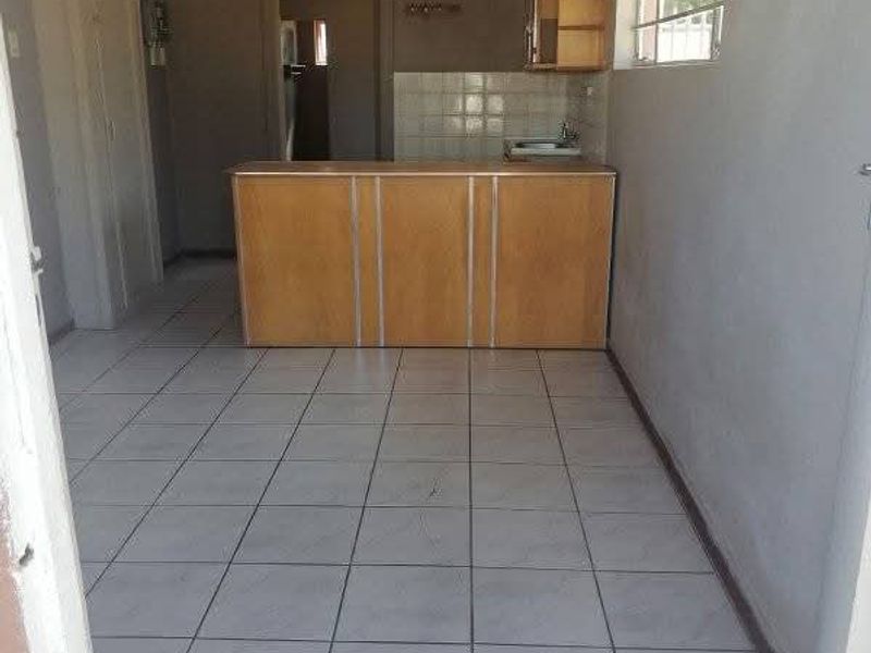 An empty kitchen area featuring tiled flooring, built-in cabinetry with a sink, and a tiled splashback, offering a blank canvas for renovation.