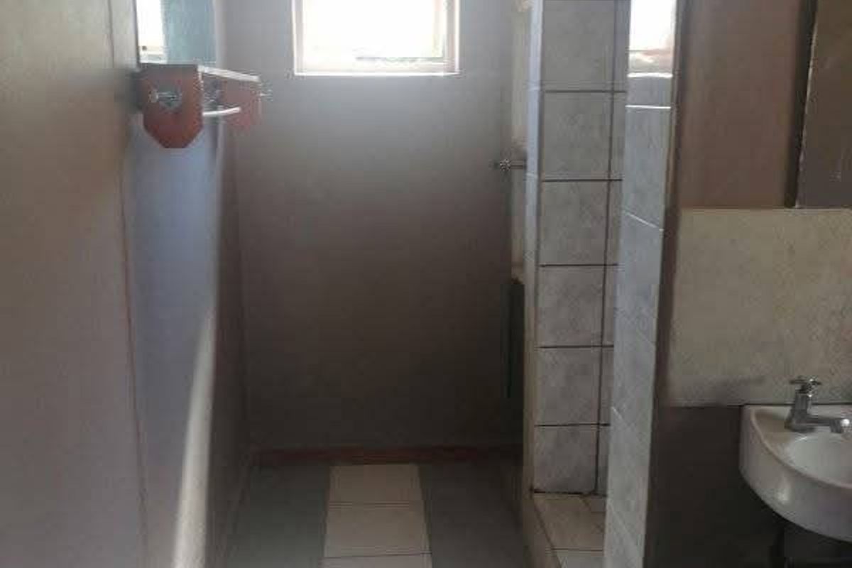 A functional bathroom featuring a shower enclosure, wall-mounted basin, and tiled flooring, offering a blank canvas for potential modernization and renovation.