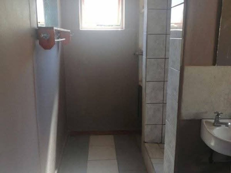 A functional bathroom featuring a shower enclosure, wall-mounted basin, and tiled flooring, offering a blank canvas for potential modernization and renovation.