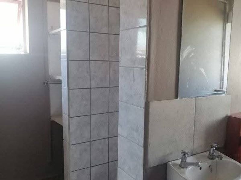 A functional bathroom featuring a tiled shower enclosure and a wall-mounted basin with a mirror, requiring cosmetic updates to improve its overall condition.