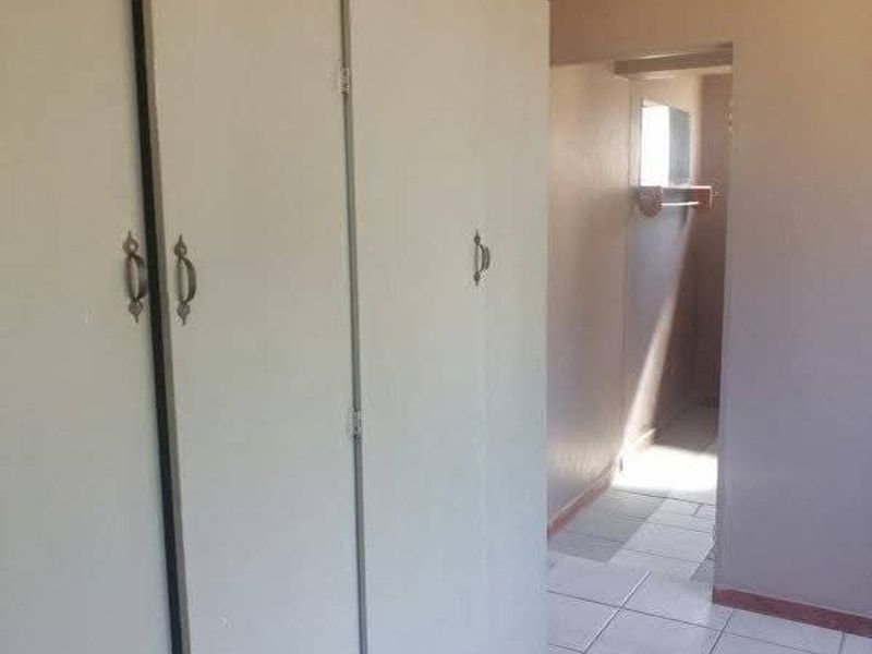 A bedroom featuring built-in cupboards and tiled flooring, with a view leading into an adjacent hallway area.