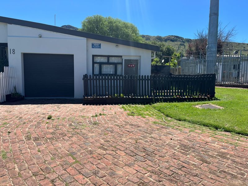 Front exterior view of the property featuring a brick paved driveway, garage, and a small fenced garden area.