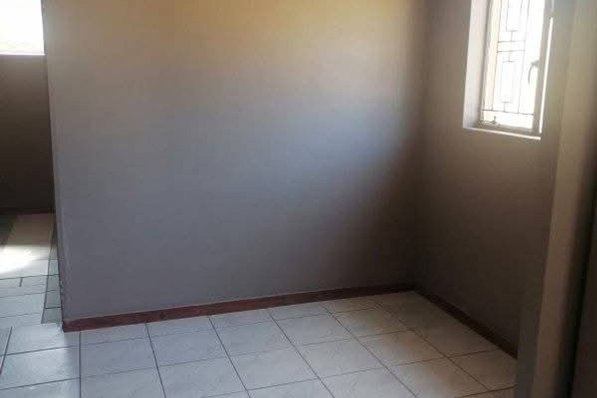 An empty bedroom featuring tiled flooring, neutral wall paint, and a window fitted with security bars.