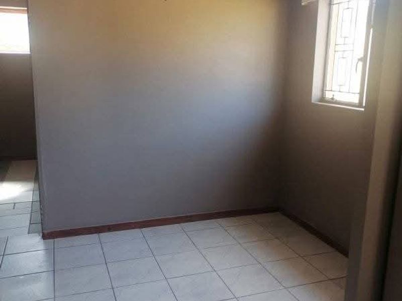 An empty bedroom featuring tiled flooring, neutral wall paint, and a window fitted with security bars.