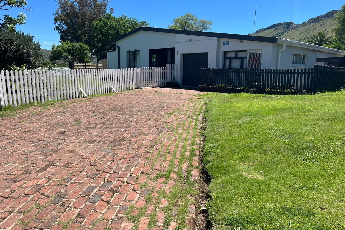 Front exterior view of the property featuring a brick driveway, white picket fencing, and a single garage door.