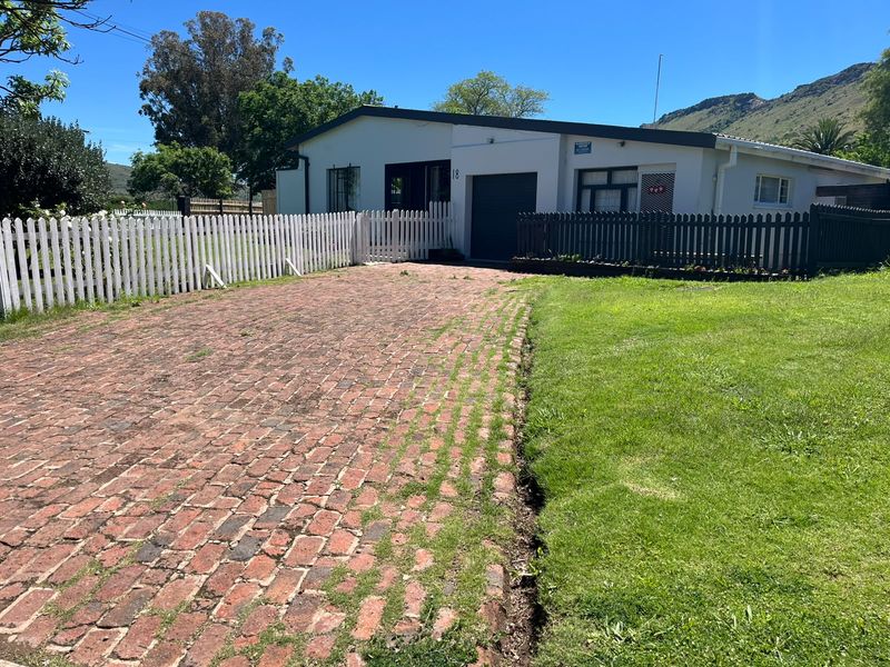 Front exterior view of the property featuring a brick driveway, white picket fencing, and a single garage door.