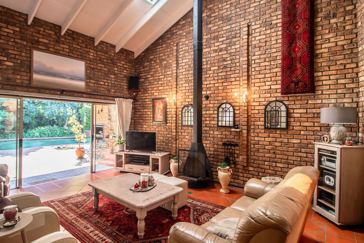Spacious living room featuring exposed brick walls, a vaulted ceiling with skylight, a central freestanding fireplace, and sliding doors opening to the pool area.