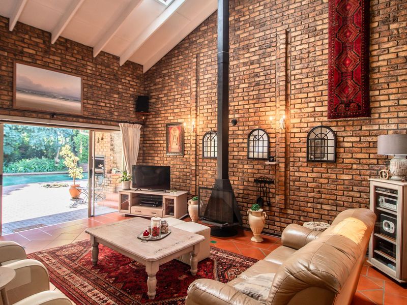 Spacious living room featuring exposed brick walls, a vaulted ceiling with skylight, a central freestanding fireplace, and sliding doors opening to the pool area.