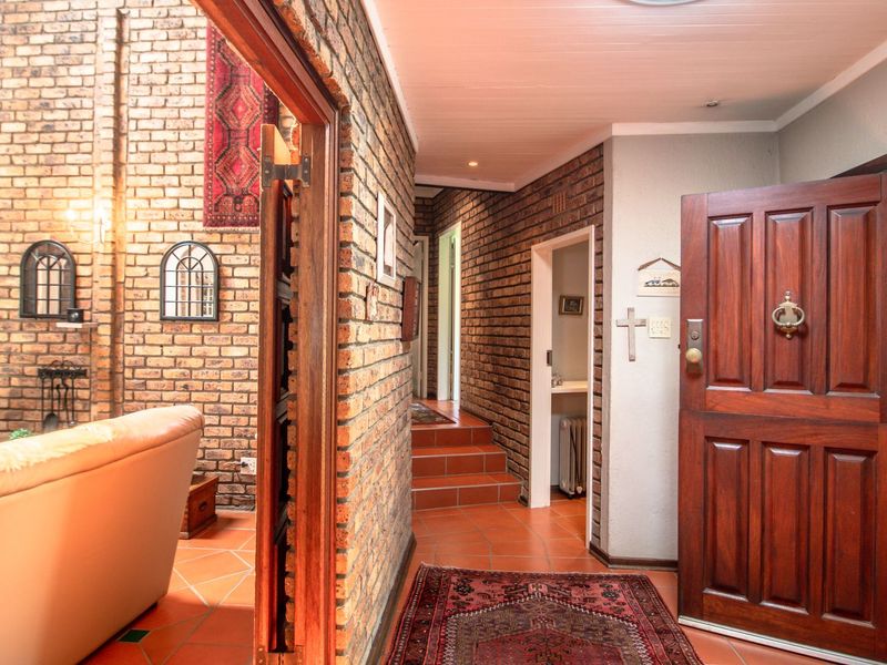 Welcoming entrance hall featuring exposed brickwork, terracotta-style tiled flooring, and a direct view into the adjacent living area with a built-in fireplace.