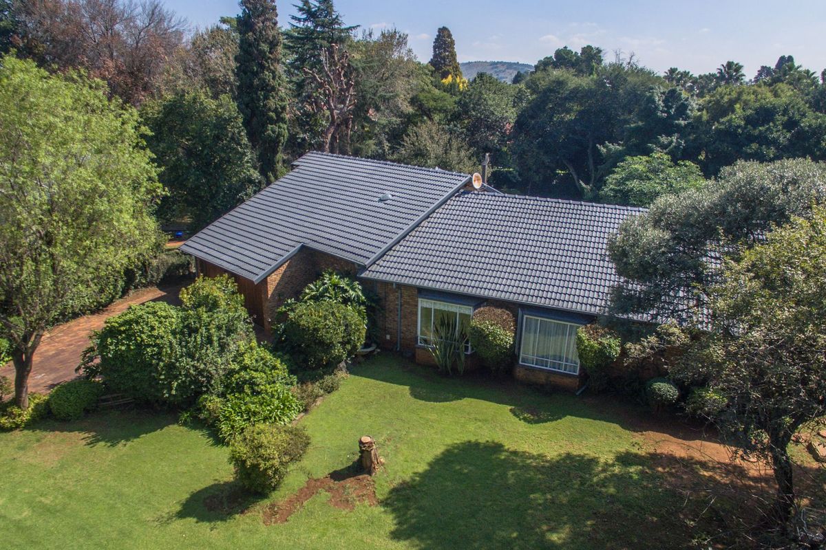 Aerial view of a single-story brick house with a tiled roof, surrounded by a spacious, well-established garden and mature trees.