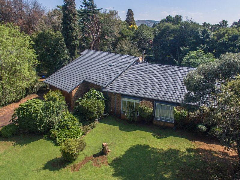 Aerial view of a single-story brick house with a tiled roof, surrounded by a spacious, well-established garden and mature trees.