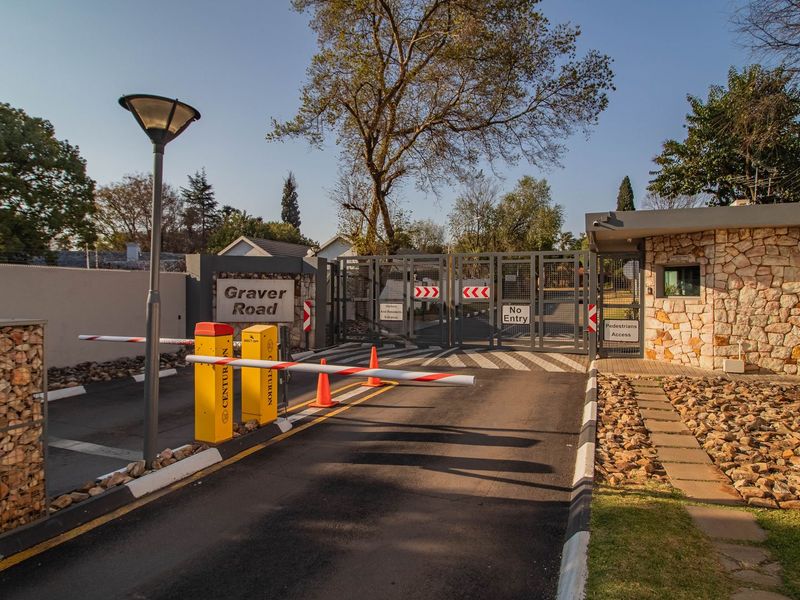 Secure gated entrance to the property featuring a boom gate, pedestrian access, and stone-clad guard house.