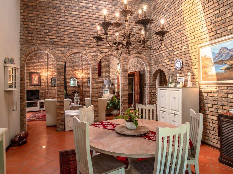 A characterful dining room featuring exposed brick walls, elegant arched doorways, terracotta flooring, and a classic wrought iron chandelier.