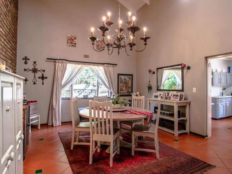 Spacious dining room featuring a vaulted ceiling, exposed brick accent wall, and classic terracotta floor tiles, with an adjacent view into the kitchen area.