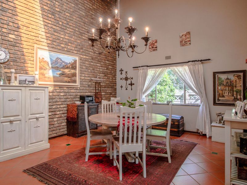 A dining room featuring a prominent exposed brick wall, terracotta floor tiles, and a classic wrought iron chandelier, creating a warm and rustic atmosphere.