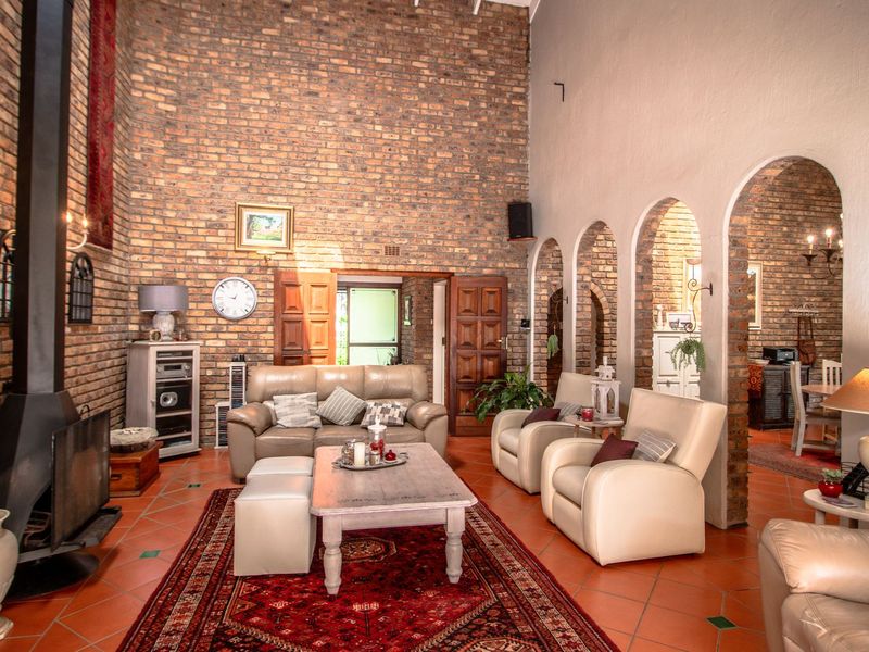 Spacious living room featuring high ceilings, exposed brick walls, a prominent freestanding fireplace, and classic terracotta floor tiles with arched architectural details.