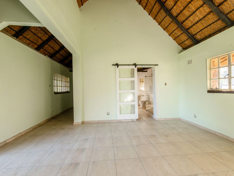 Spacious bedroom featuring high vaulted ceilings with exposed thatch, tiled flooring, and a sliding barn door leading to an en-suite bathroom.