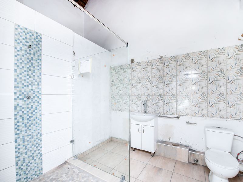 A bathroom featuring a glass shower screen, pedestal vanity, and toilet, currently requiring significant renovation and finishing of wall surfaces and tiling.
