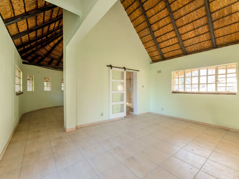Spacious living area featuring high vaulted ceilings with exposed thatch and timber rafters, tiled flooring, and a sliding barn door.