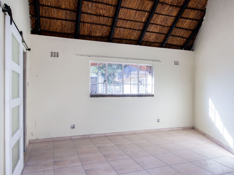 An empty bedroom featuring a high-volume thatched roof with exposed rafters, tiled flooring, and a sliding barn-style door.