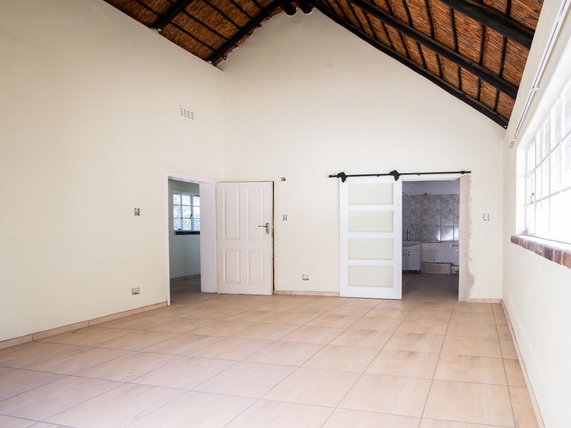 Spacious bedroom featuring high exposed thatch ceilings, tiled flooring, and a sliding barn door leading to an en-suite bathroom.