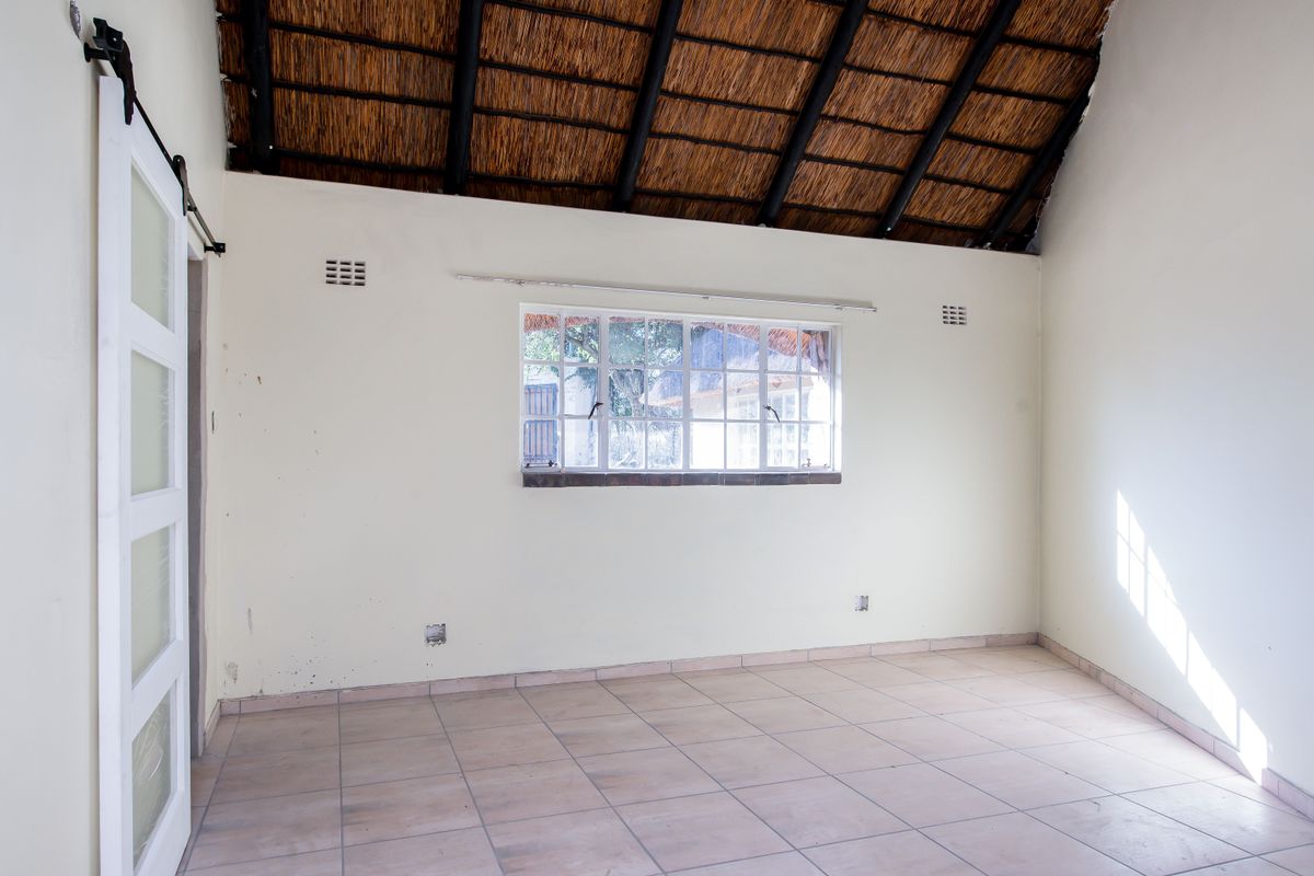 An empty bedroom featuring a high-volume thatched roof with exposed rafters, tiled flooring, and a sliding barn-style door.
