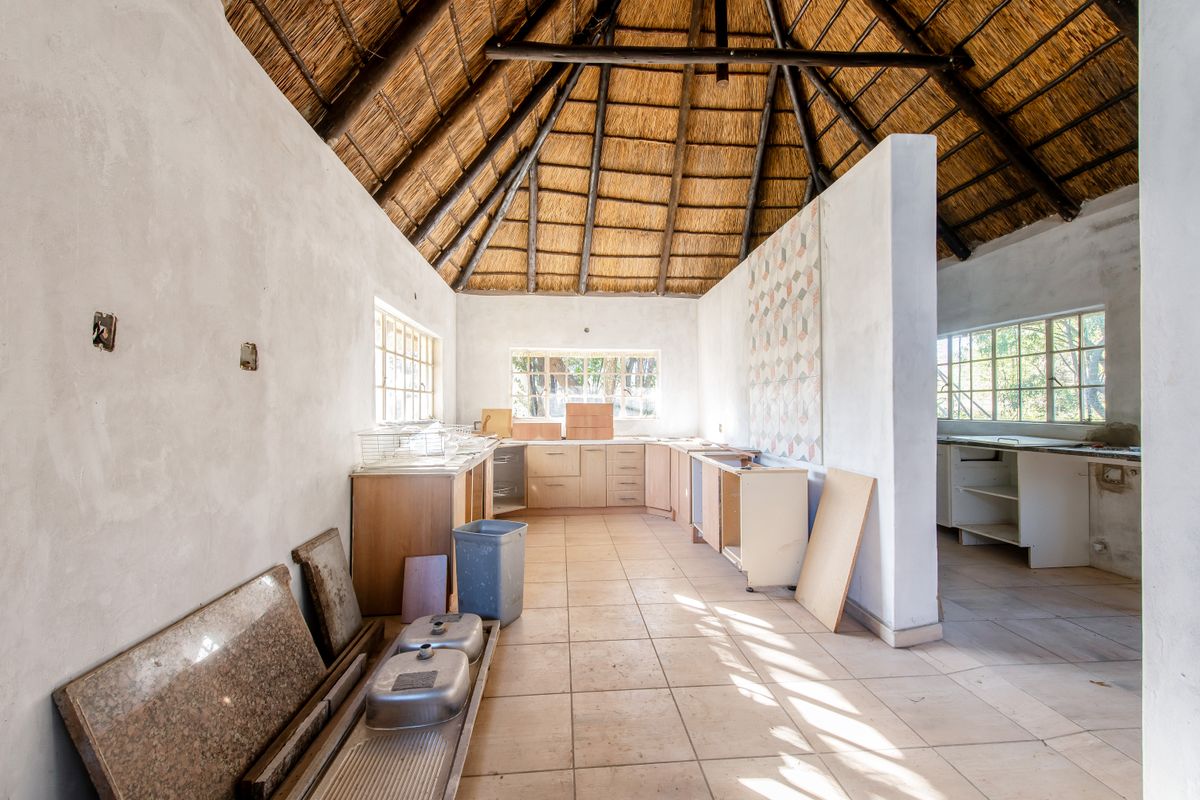 Spacious kitchen area featuring a high thatched roof with exposed rafters, tiled flooring, and unfinished cabinetry awaiting final installation and completion.