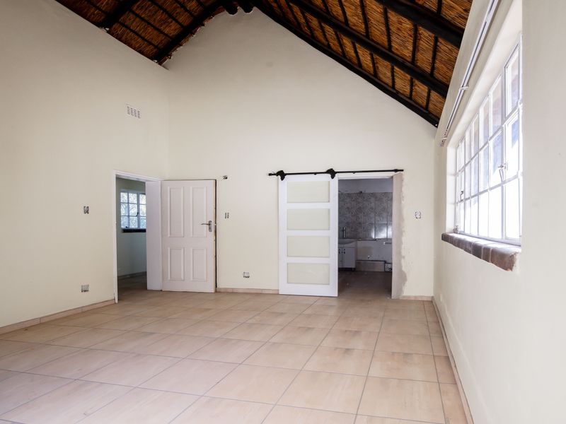 Spacious bedroom featuring a high vaulted thatched ceiling with exposed rafters, tiled flooring, and a sliding barn door leading to an en-suite bathroom.
