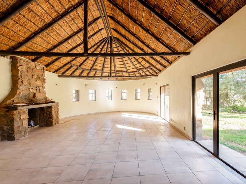 Spacious living area featuring a high vaulted thatched ceiling with exposed timber trusses, a rustic stone fireplace, and large sliding doors opening to the garden.