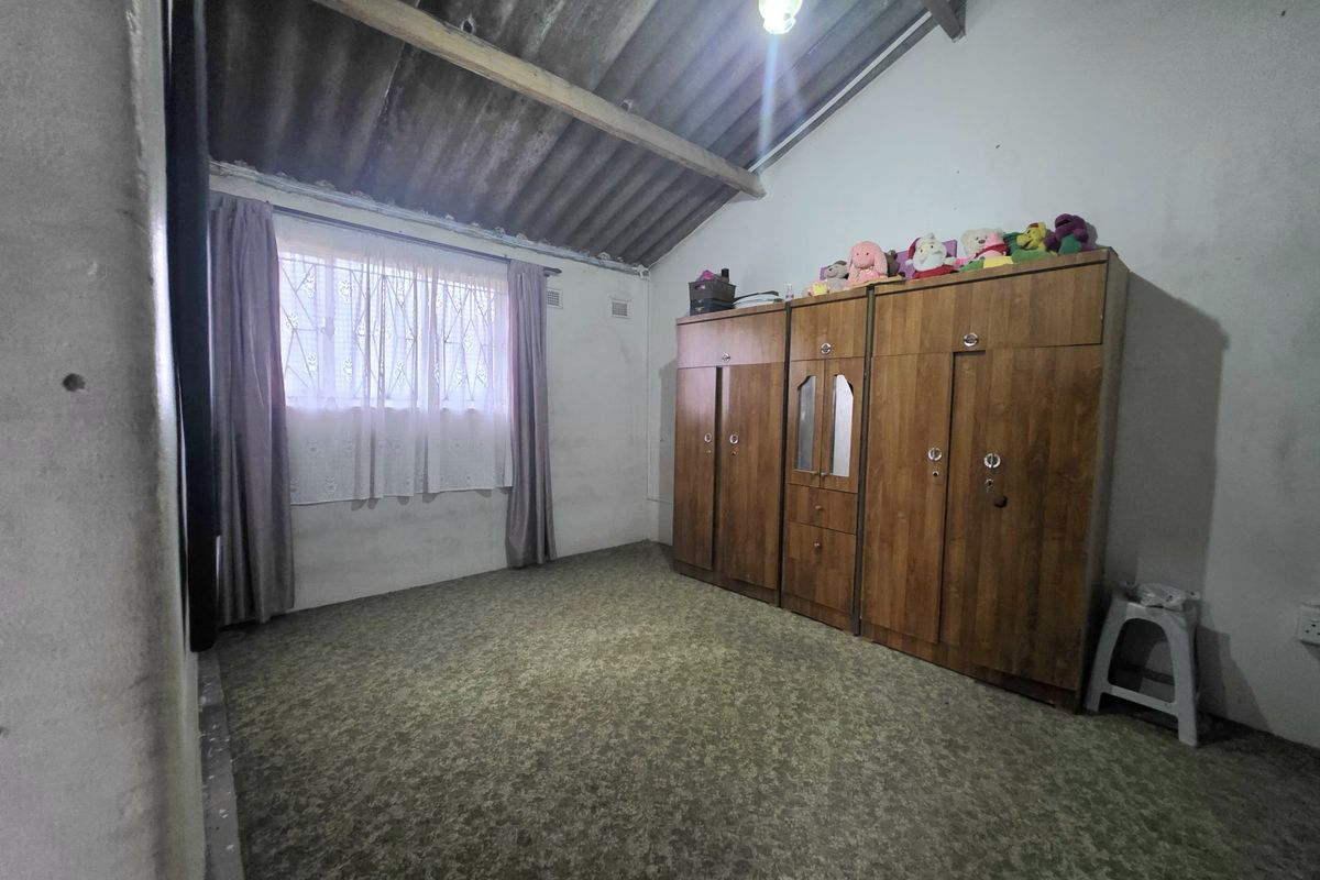 A bedroom featuring exposed roof rafters, corrugated ceiling, and carpeted flooring, requiring cosmetic updates to improve the overall finish and appeal.