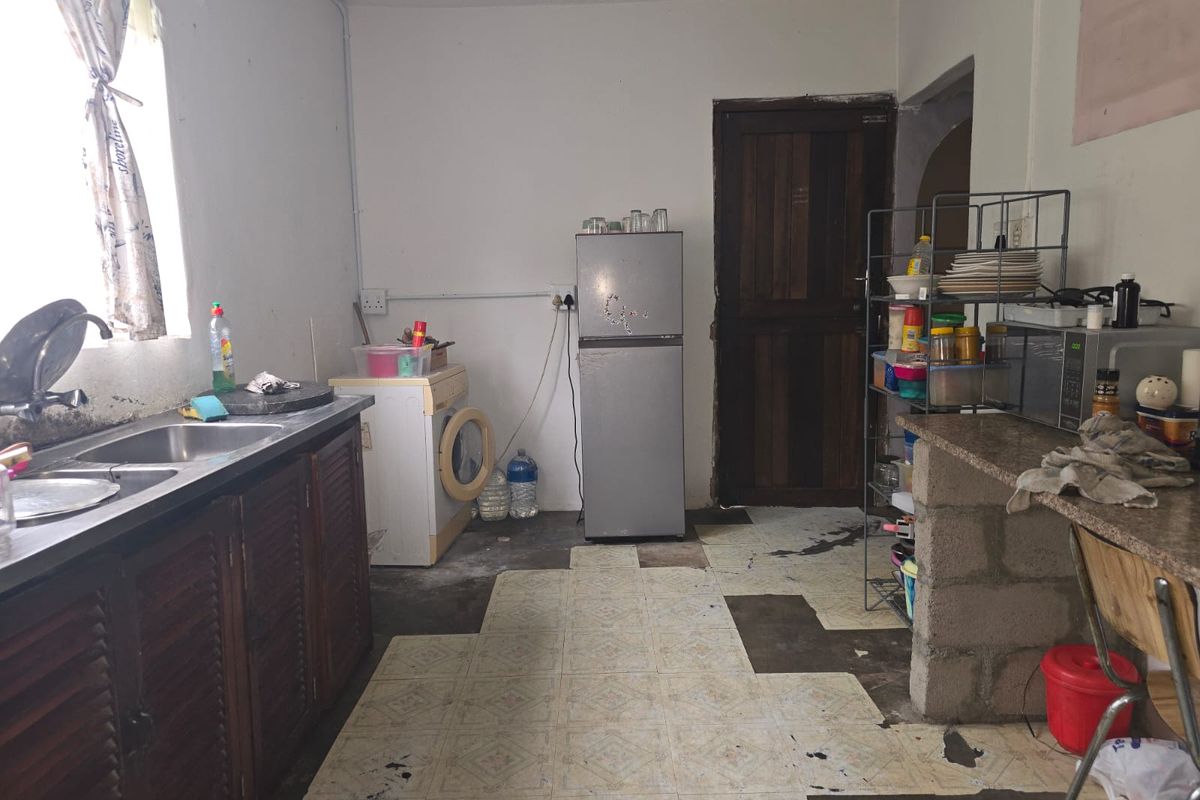 A dated kitchen area featuring a double bowl sink, louvered cabinetry, and a masonry breakfast bar, requiring significant renovation and cosmetic updates.