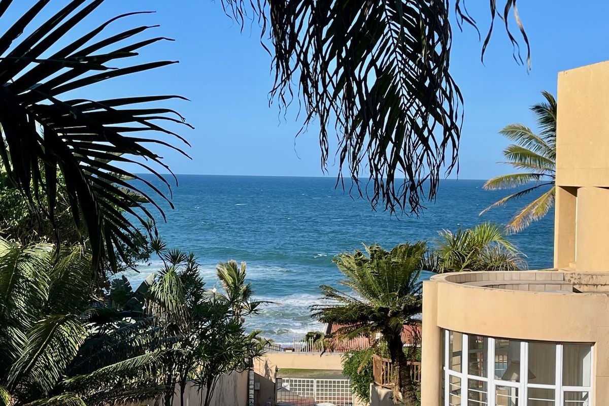 A scenic view of the ocean framed by palm trees, featuring a modern curved building facade with large windows.