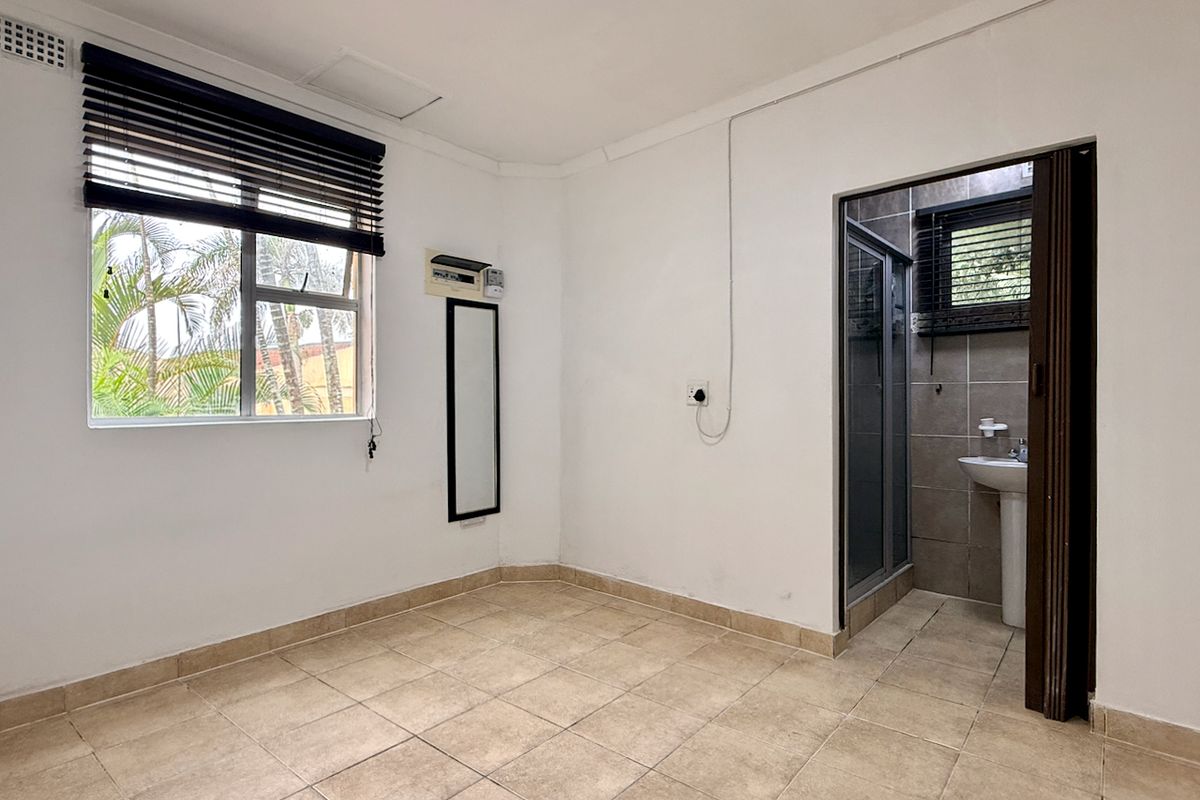 A vacant bedroom featuring tiled flooring, an air conditioning unit, and an attached en-suite bathroom with a shower and pedestal basin.
