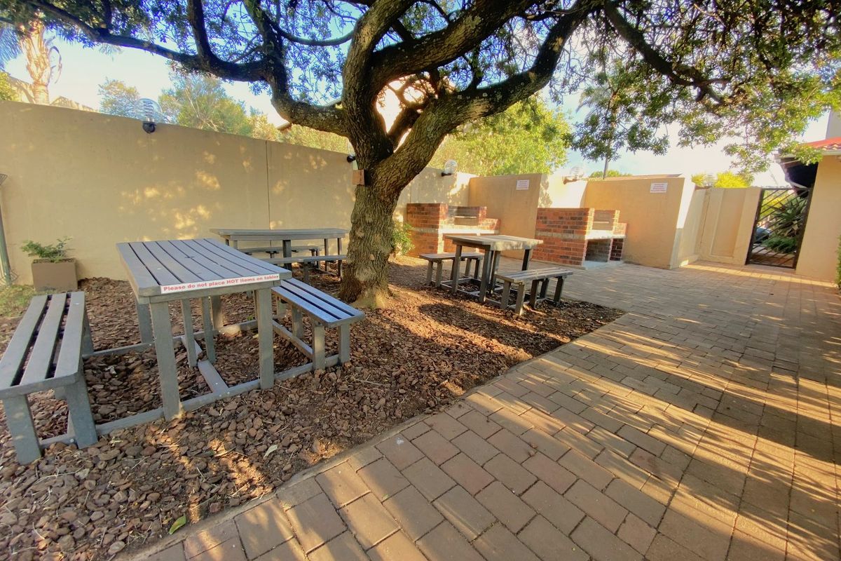 Outdoor communal braai and picnic area featuring brick-built barbecue stations, paved flooring, and mature shade trees within a secure walled courtyard.