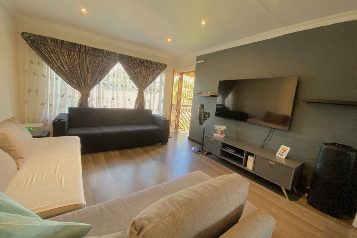 A comfortable living room featuring wood-look flooring, recessed ceiling lighting, and a dark accent wall with integrated television mounting.