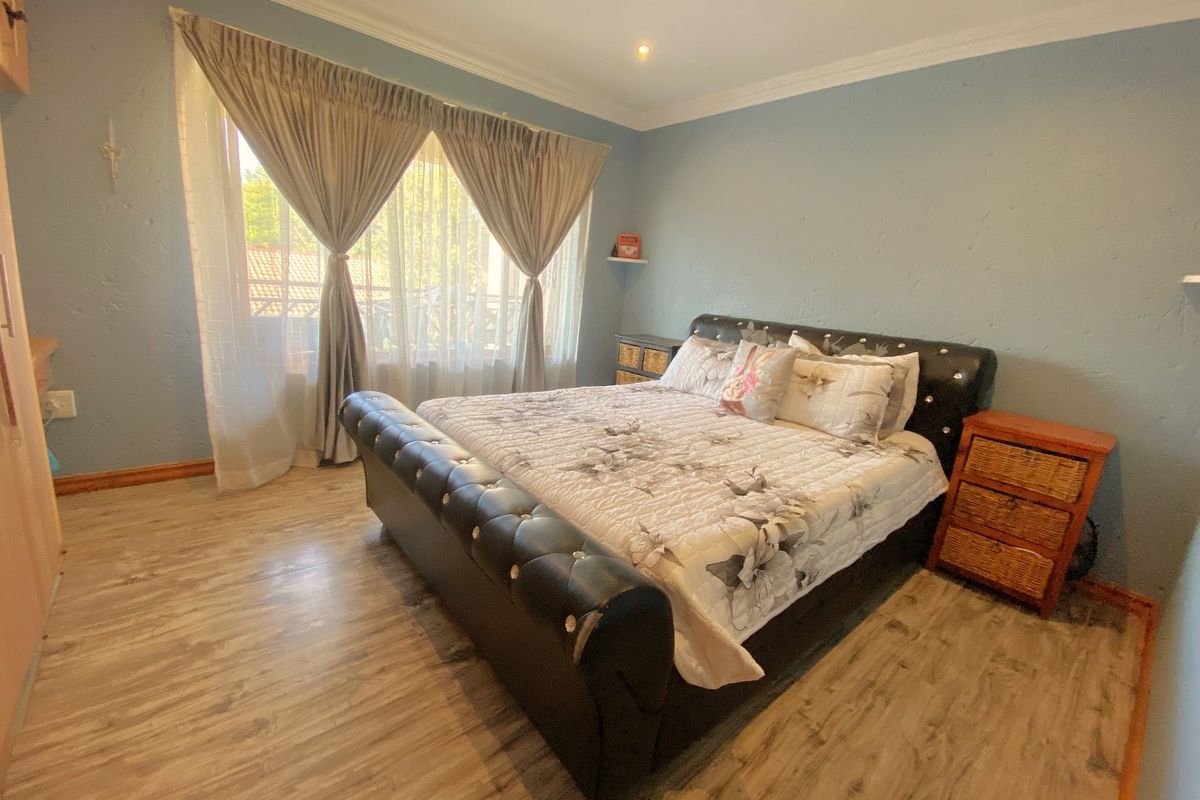 A well-lit bedroom featuring wood-look laminate flooring, crown molding, and a large window with curtain tracks.