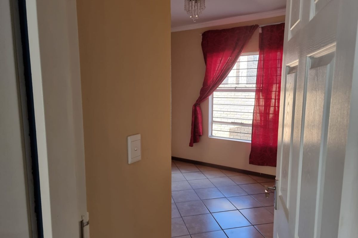 A view into an empty bedroom featuring tiled flooring, a window with security bars, and a central ceiling light fixture.