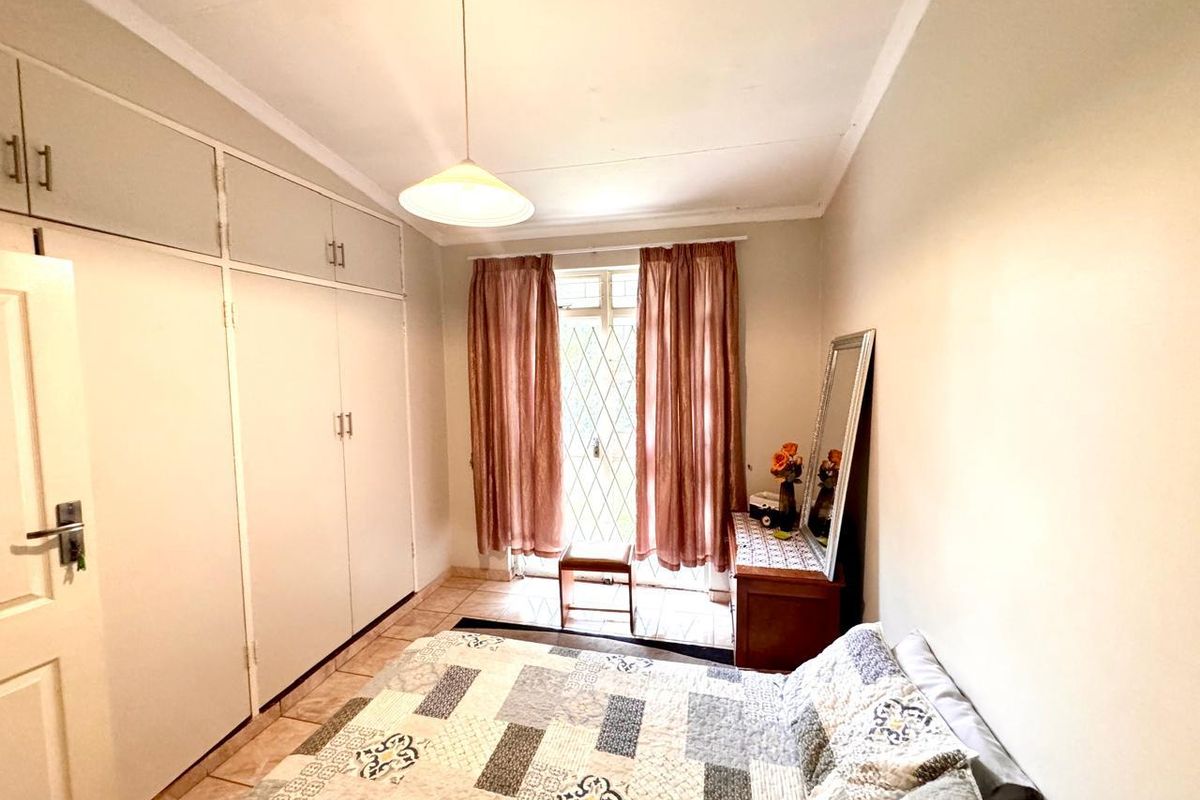 A functional bedroom featuring built-in cupboards, tiled flooring, and a security gate leading to an outdoor area.