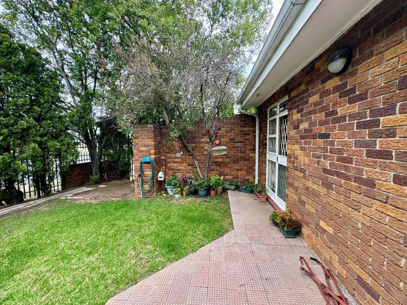 A rear exterior view of the townhouse featuring a brick facade, a paved patio area, and a small private garden space.