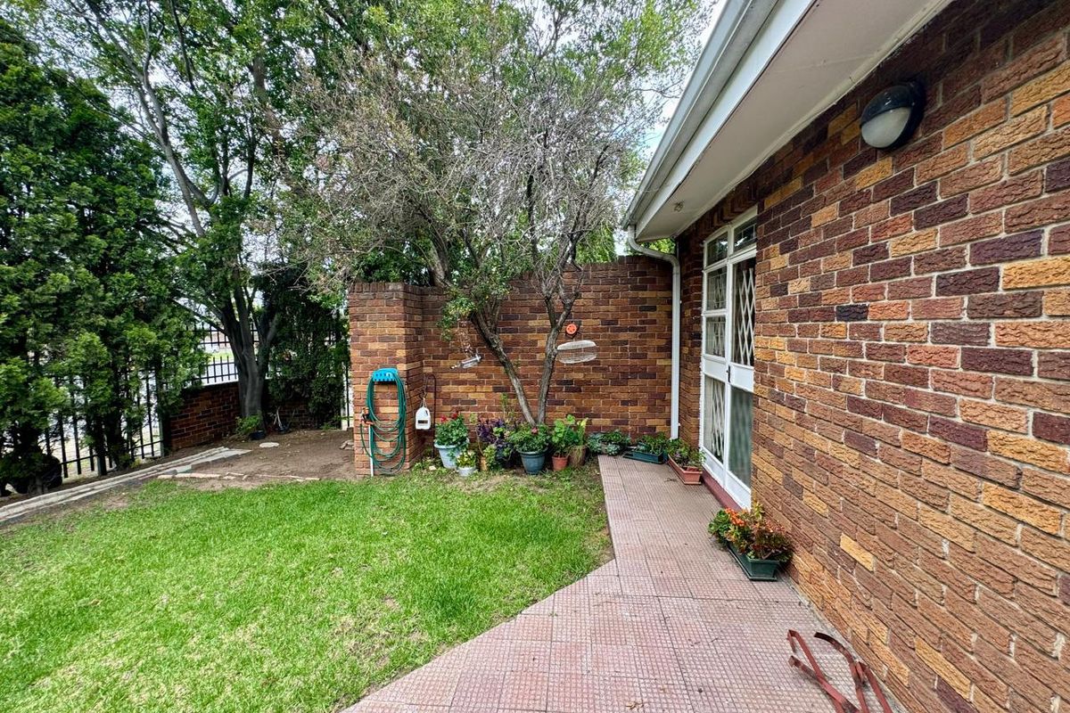 A rear exterior view of the townhouse featuring a brick facade, a paved patio area, and a small private garden space.
