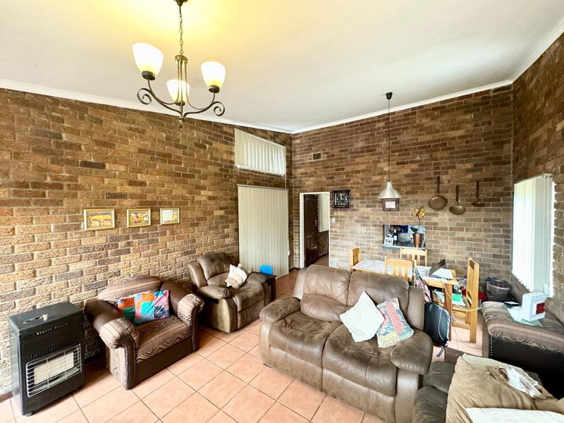 Spacious open-plan living and dining area featuring exposed brick walls, vaulted ceilings, and tiled flooring, offering a rustic aesthetic with potential for modernization.