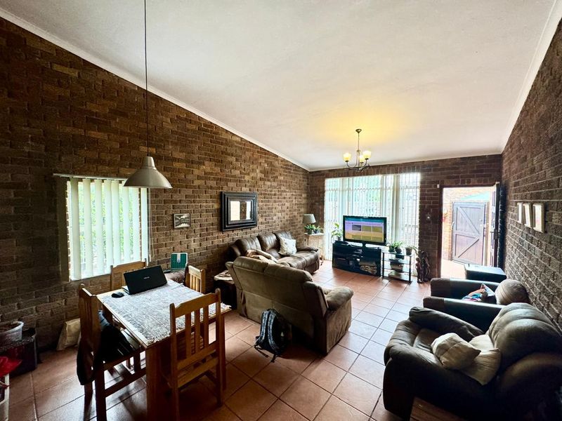 Spacious open-plan living and dining area featuring exposed brick walls, tiled flooring, and a vaulted ceiling with direct access to the exterior.