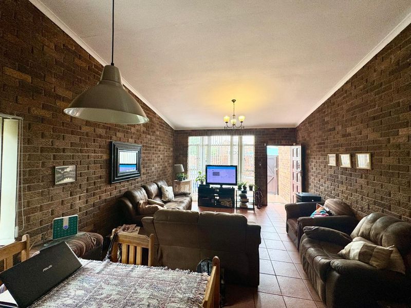 Spacious living room featuring exposed brick walls, tiled flooring, and natural light through a sliding glass door leading to the exterior.