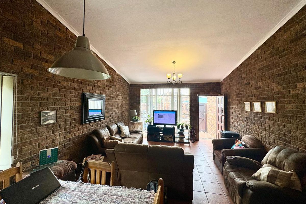 Spacious living room featuring exposed brick walls, tiled flooring, and natural light through a sliding glass door leading to the exterior.